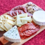 cheese plate with cured meats on a red tablecloth