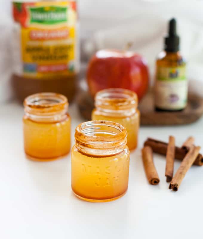 3 chupitos de vinagre de sidra de manzana en una mesa con canela y manzana