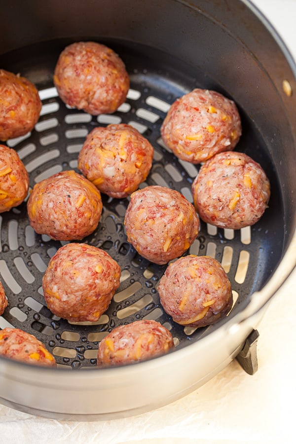 Raw sausage balls aligned in an air fryer basket ready to be cooked.