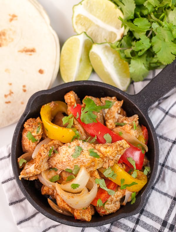 Instant Pot Chicken Fajitas in a cast iron skillet on a black and white table cloth surrounded by a lime and tortilla