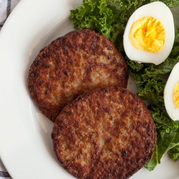 two sausage patties and a hard boiled egg sliced open all on a bed of kale on a white plate