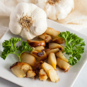 roasted garlic cloves on a plate with a head of garlic