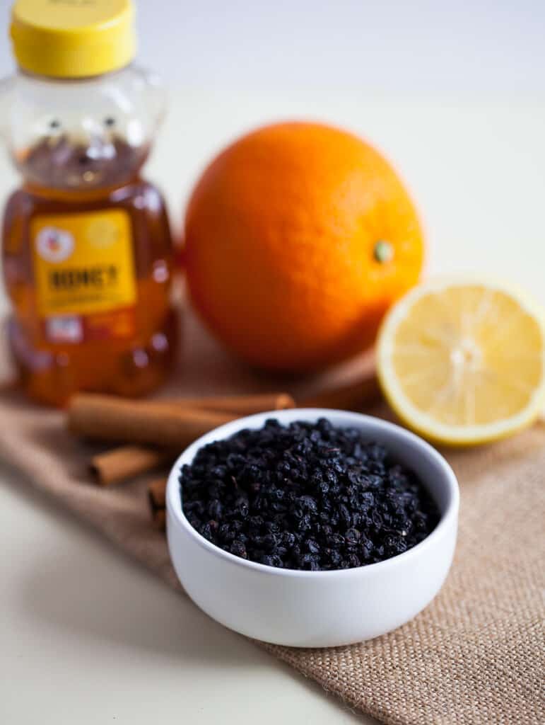 a white bowl of dried elderberries with honey and orange in the background