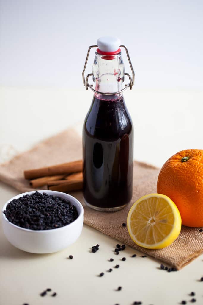 a picture of eldeberry syrup in a glass bottle with oranges and dried elderberries.