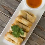 air fryer cooked lumpia on a white plate, next to dipping sauce