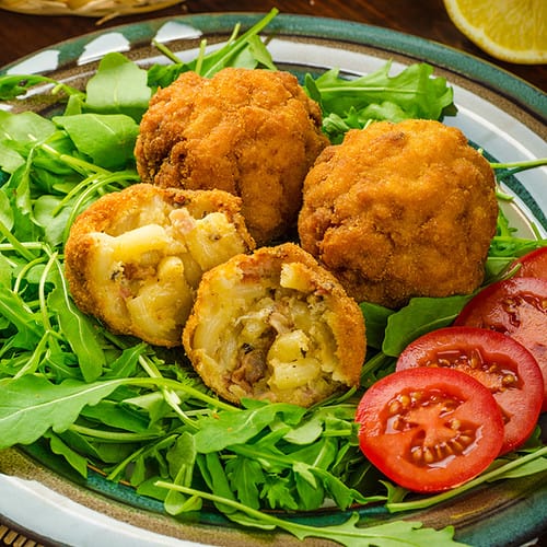 macaroni and cheese balls on a plate with tomato and arugula