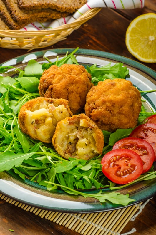 macaroni and cheese balls on a plate with tomato and arugula