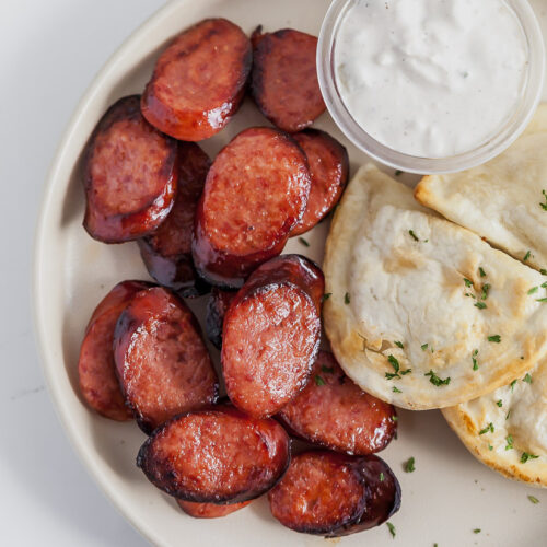 sliced smoked sausage on a plate with pierogies and sour cream