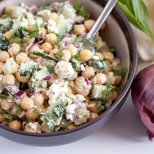 salad in a bowl with chickpeas, cucumbers, and feta cheese with a spoon