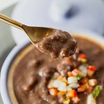 black bean soup on a spoon with a bowl of black bean soup underneath